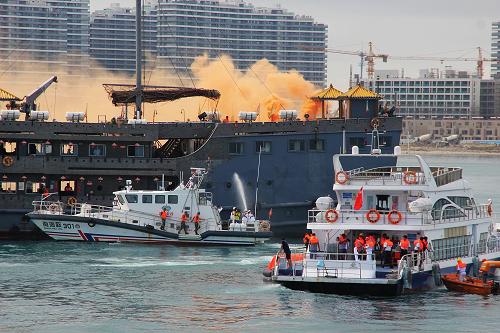 6月18日,在海南三亚海域演习现场,模拟海上救援和灭火同时进行。当日,2014年三亚大型游客船海上消防救生演习在海南省三亚海域举行。针对三亚地区海上旅游客运船舶大型化,项目多样化的特点,演习凸显船舶自救应变环节,演习了包括险情处置及应急响应、弃船、伤员转运、落水人员搜寻等课目。通过演习锻炼了船舶如何在第一时间开展自救行动,力争最大限度地降低人员和财产损失。新华社发(袁永东 摄)
